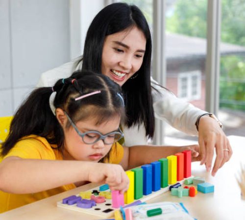 Asian girl with Down's syndrome play puzzle toy with her teacher in classroom.